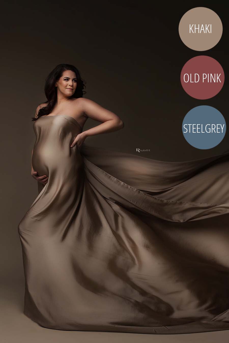 Brunette pregnant model poses wrapped in a silky scarf in khaki color. She holds her bump and her waist and looks to the side,