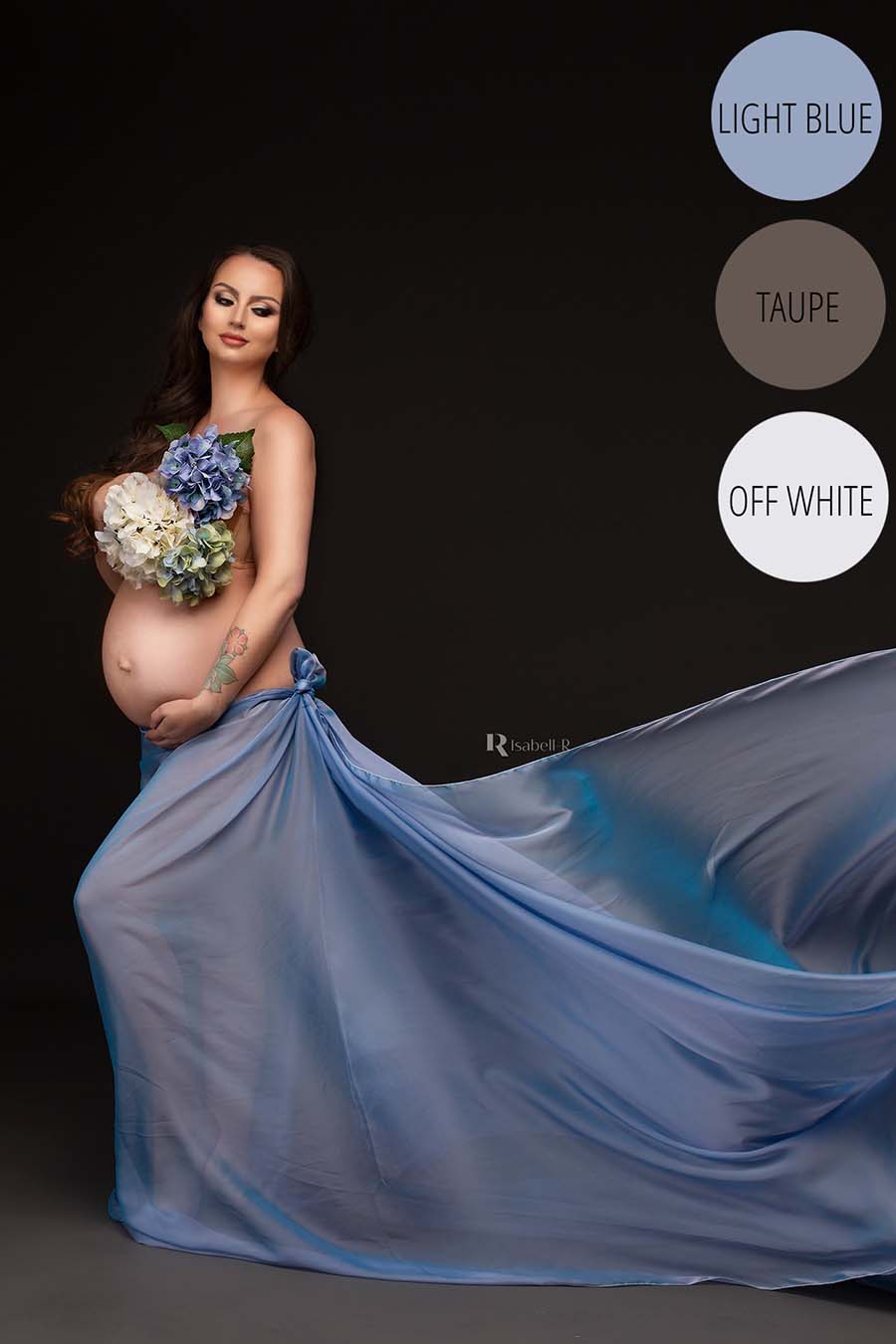 Pregnant brunette poses in a studio for a maternity photo session. She has a draping light blue fabric tied to her waist and holds a flower bouquet in front of her chest to cover her breasts.