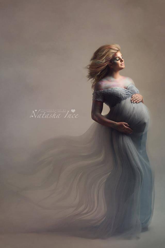 Pregnant model with blond hair poses with her eyes closed and wearing a light blue dress made of lace and tulle.