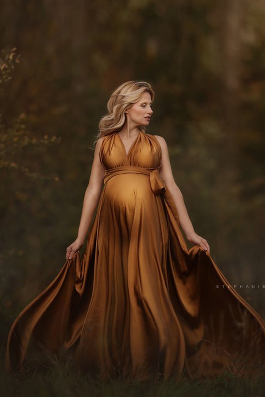 blond pregnant model poses outdoors wearing a long camel dress made of silk.