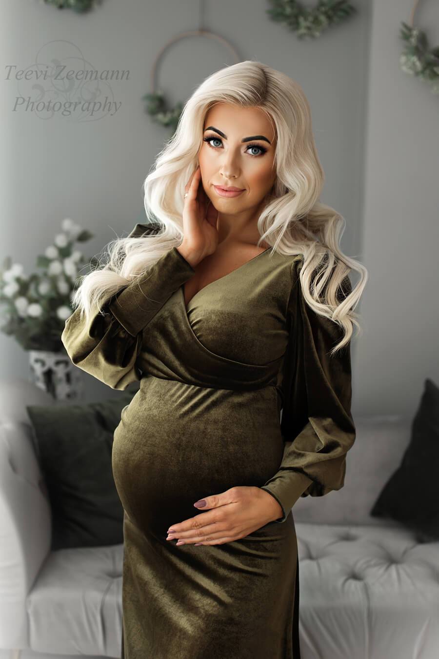 blond model poses in a studio wearing a velvet olive dress with an adjustable sweetheart top and long bishop sleeves with manchette endings.