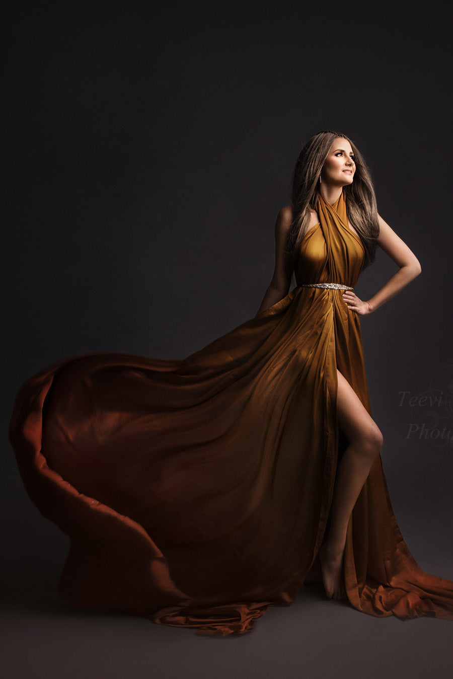 brunette model poses in a studio wearing a silky scarf in cognac tied on her body as a dress. she has a sash to match the style.