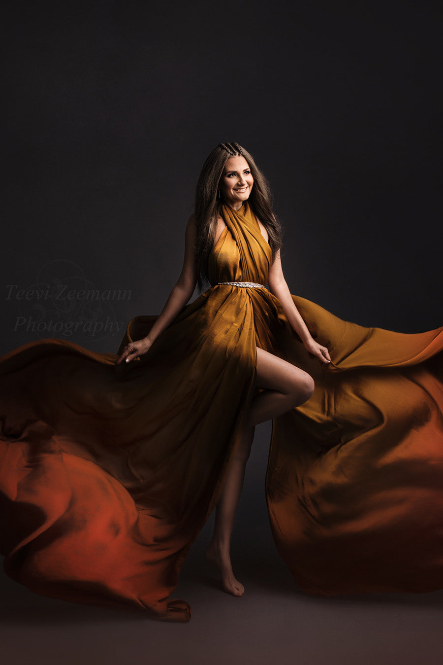 brunette model poses in a studio wearing a silky scarf in cognac tied on her body as a dress. she has a sash to match the style.