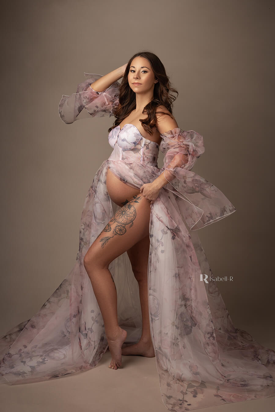pregnant model poses on her side at a studio wearing a tulle and organza dress with pattern with flowers. the dress is strapless and has attached sleeves made of organza.
