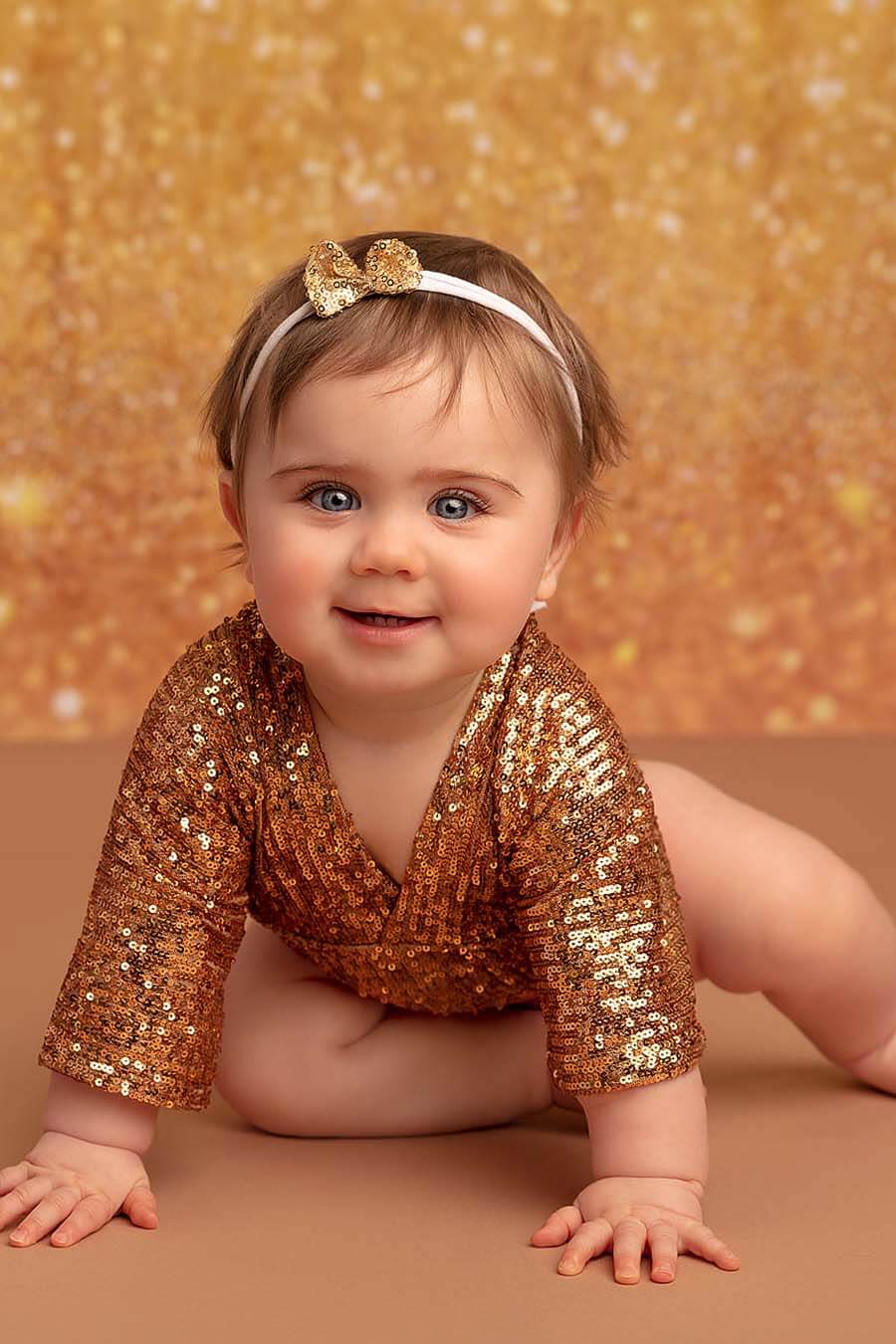 A bay is wearing a cute gold romper. And has a little hairband in the hair. 