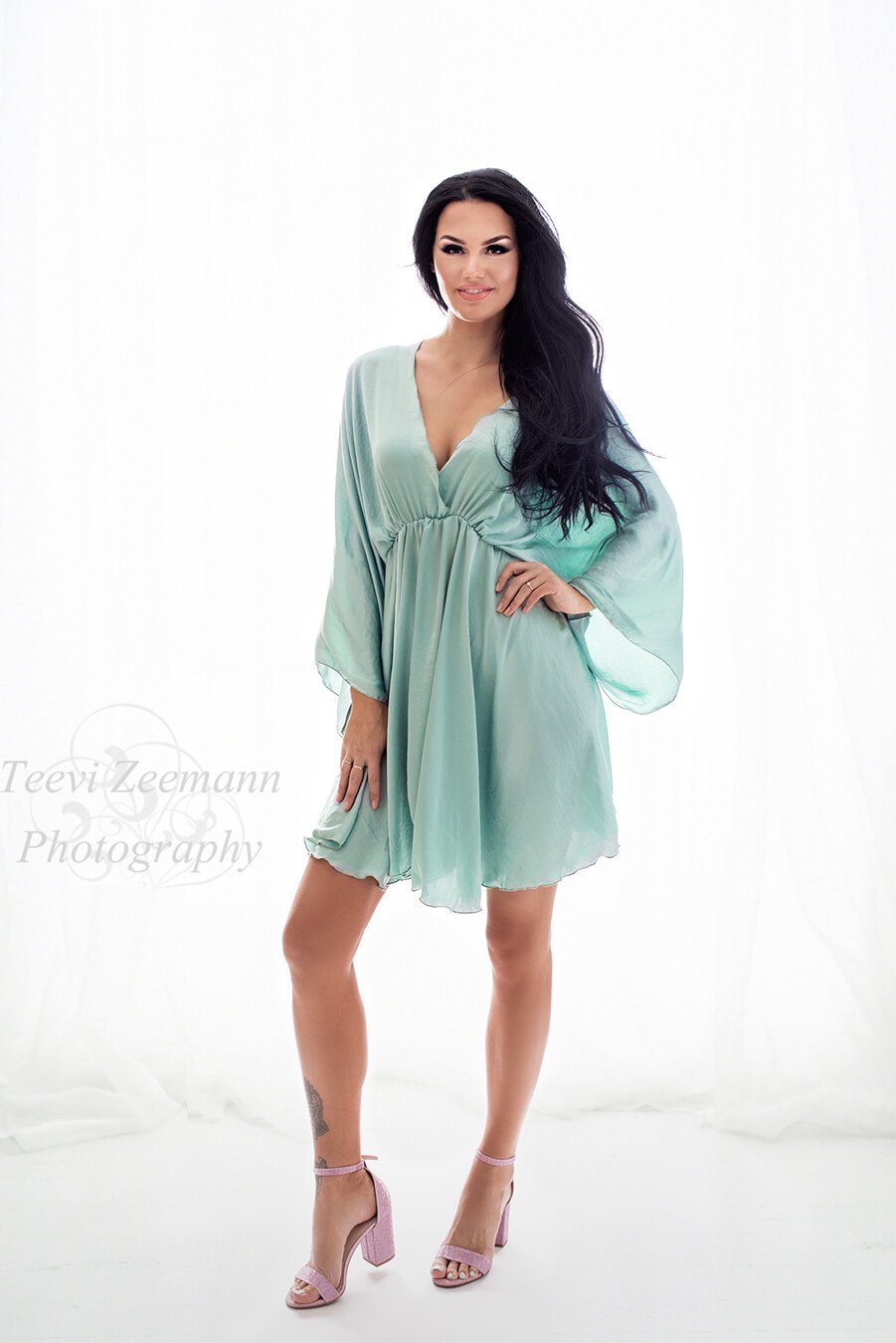 The woman is wearing a dress in the colour azur. she is standing on light purple heels. The dress has a sweetheart neckline and is tighter around the waist.