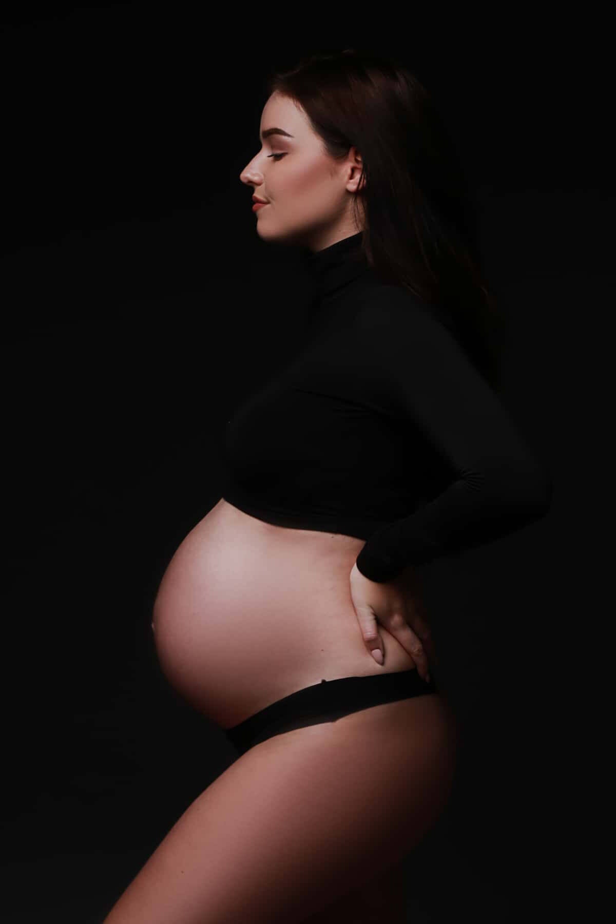 A mother to be is wearing a black long sleeved top that is showing of het belly