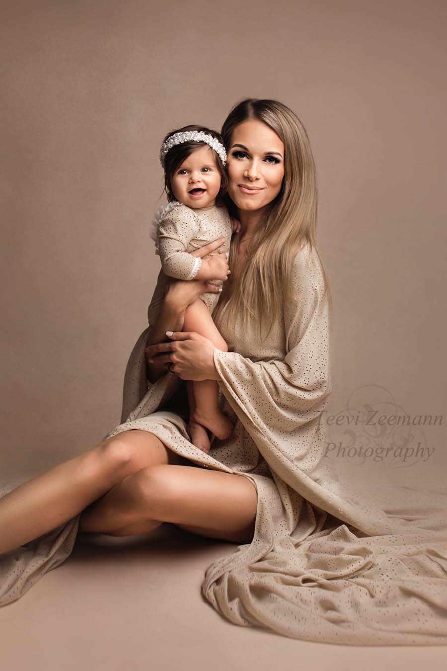 A woman is siting on the ground with her baby girl . They are wearing matching outfits. The little girl has a headband in her ahir