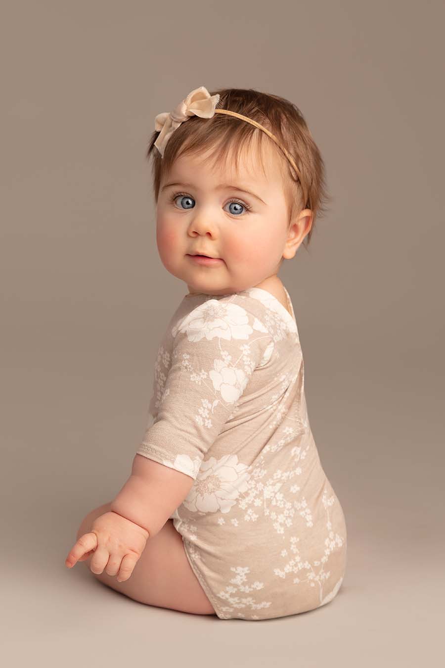 baby poses wearing a romper with long sleeves and flower pattern. she has a matching hairband.