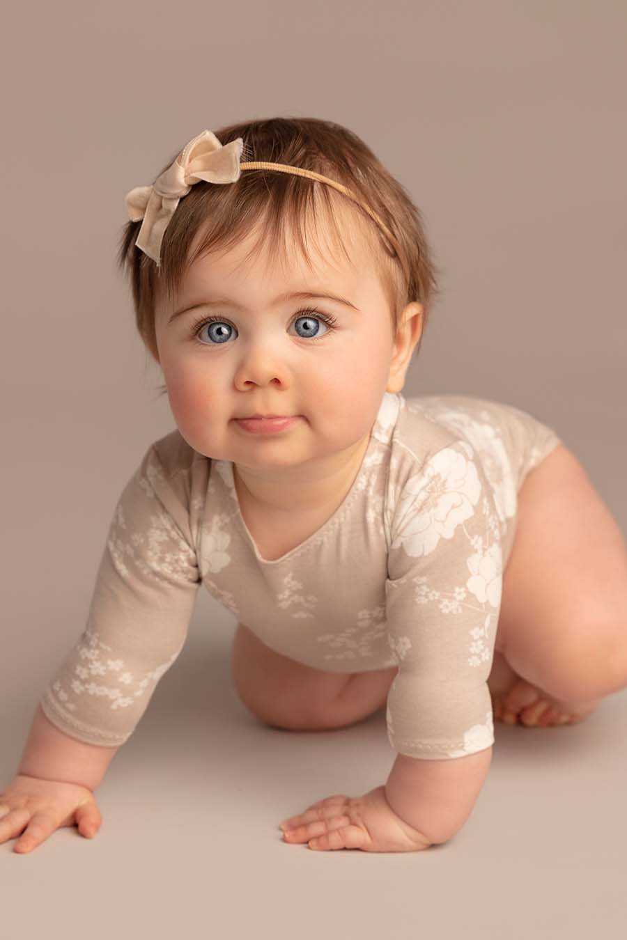 baby poses wearing a romper with long sleeves and flower pattern. she has a matching hairband.