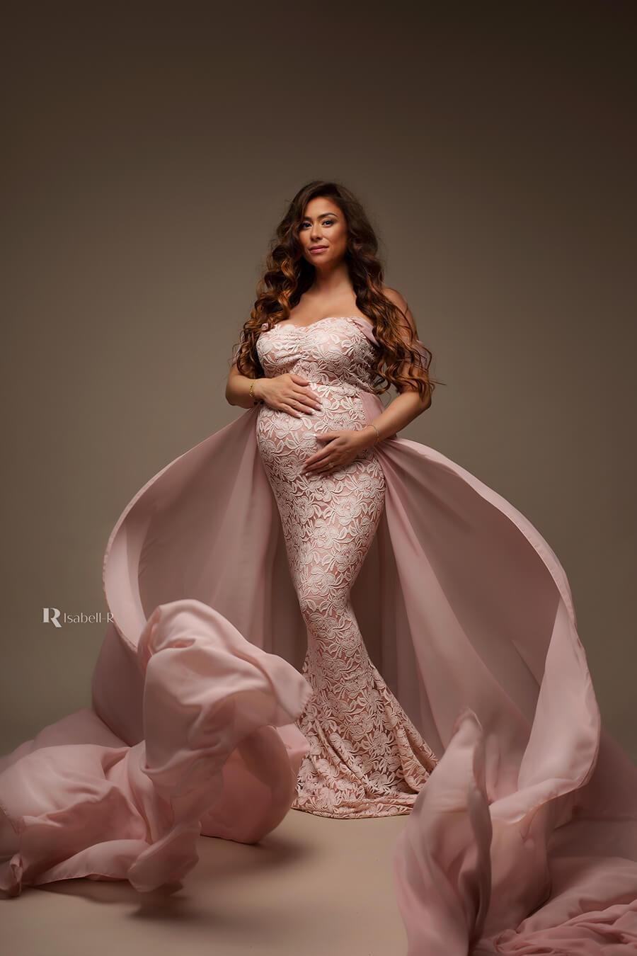 A pregnant woman is wearing a tight dress from lace material. The dress has drop sleeves. The material of the skirt is thrown in front of her