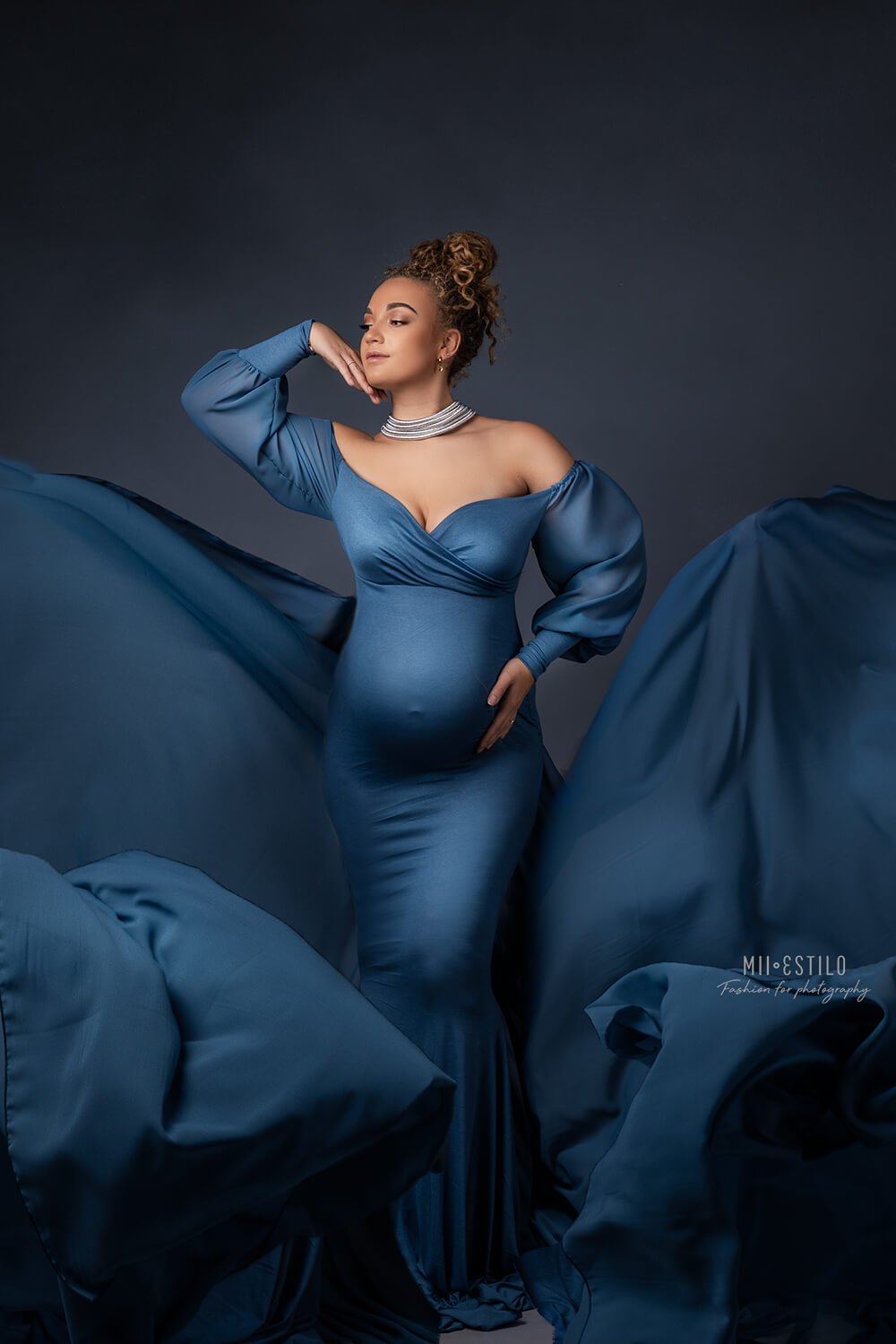 pregnant model poses in a studio wearing a long denim dress with an adjustable sweetheart top and bishop sleeves.