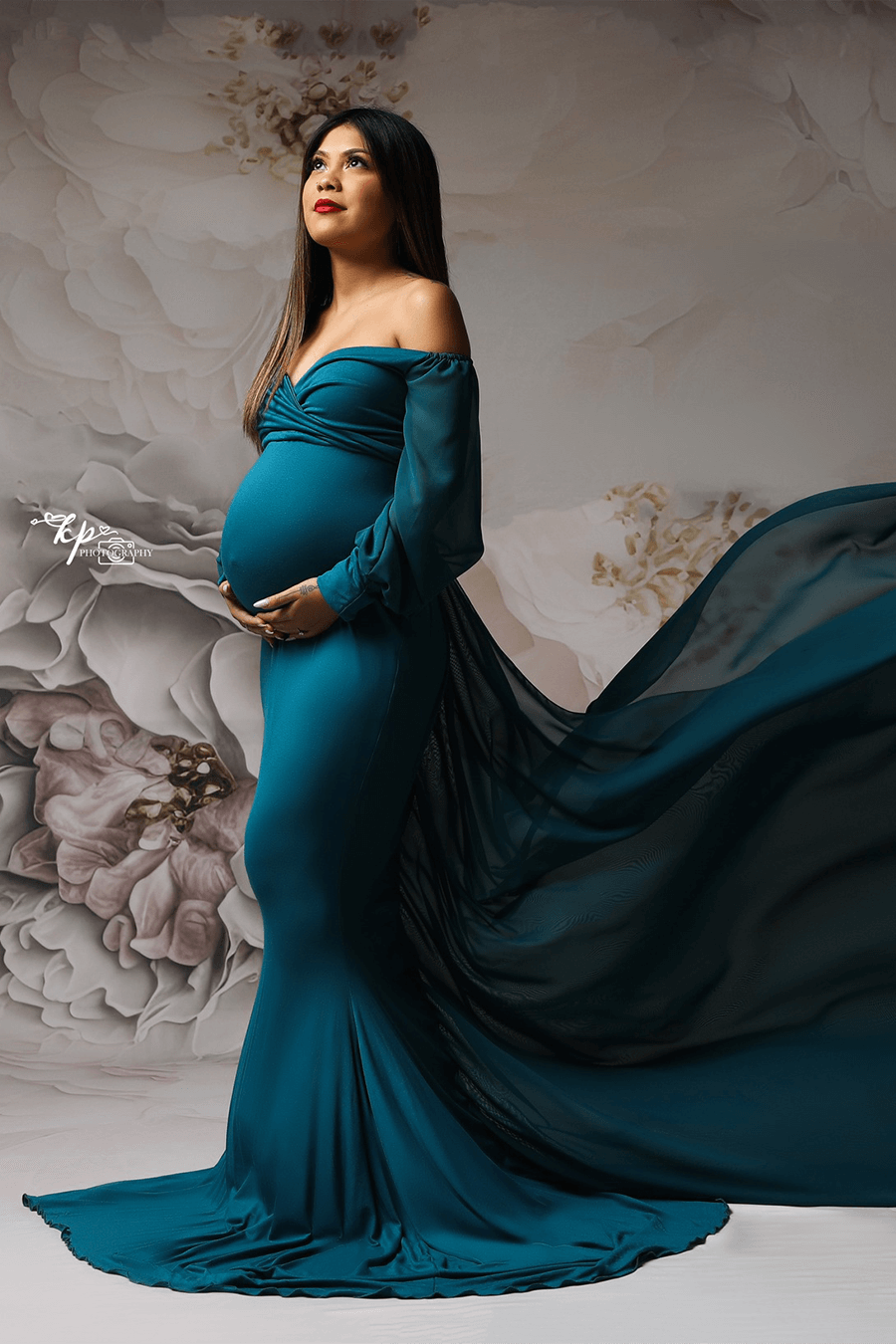 model poses in a studio wearing a petrol long dress with long chiffon sleeves. 