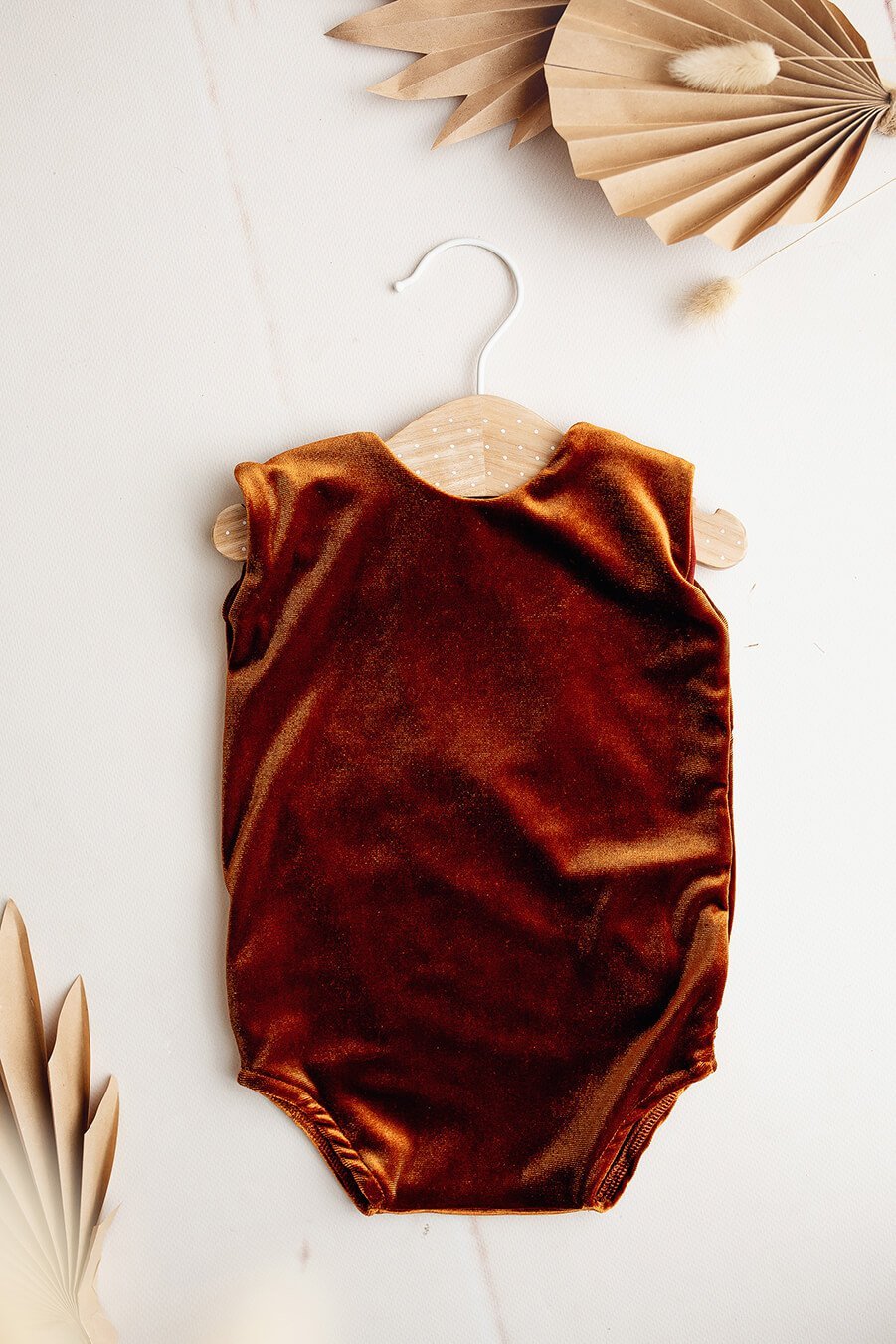 A baby romper is laying on the ground. The background is white. The colour of the romper is cognac