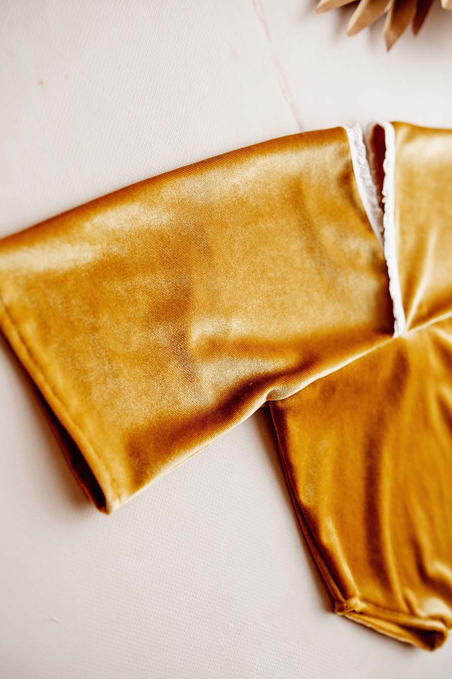 The romper is laying on a white background. It is a close up product photograph. The romper has a velours fabric and is in the color amber.
