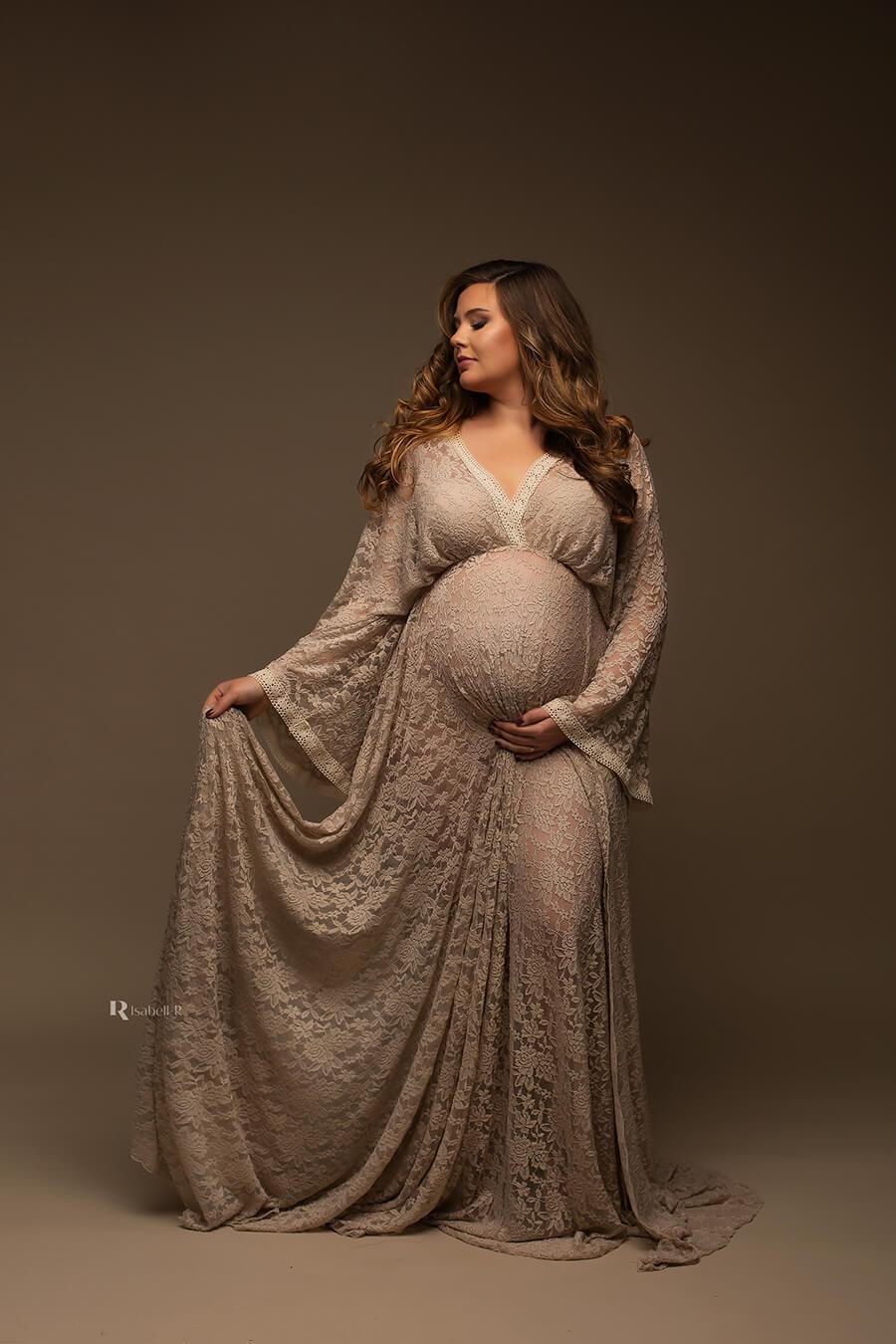 A pregnant model is wearing a BOHO styled dress in the colour sand. The dress is made of lace and the top has a low v cut neckline.