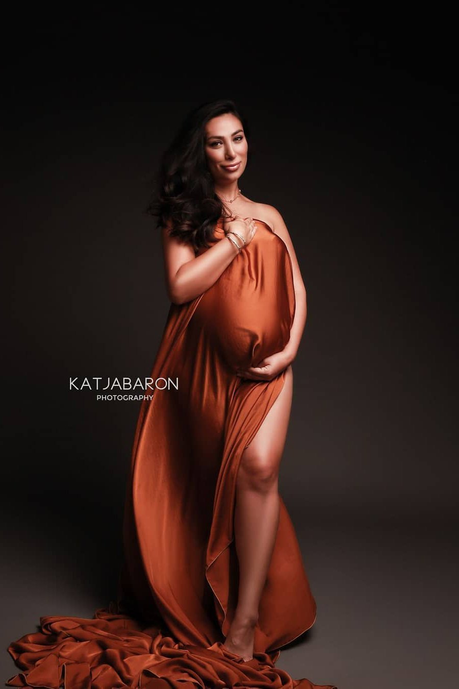 brunette model poses with a cognac scarf covering her breast and belly. she stares and smiles at the camera