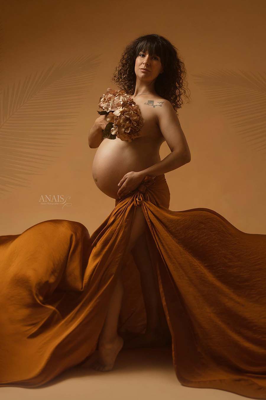 pregnant model poses with a hortensia bouquet covering her chest and with a silky scarf tight on her waist just like a skirt.