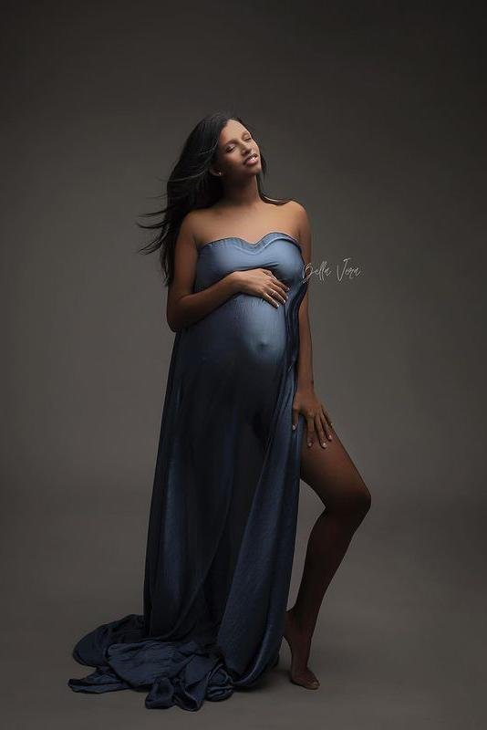 pregnant model poses in a studio wearing a piece of denim draping fabric covering her breast, belly and leg. she is facing up and has her eyes closed.