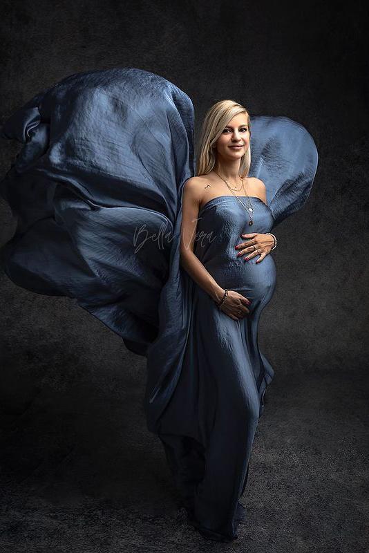 blond model poses in a studio wearing a scarf in denim color covering her belly, chest and legs. the piece is flowing on the back and the model is looking to the camera.