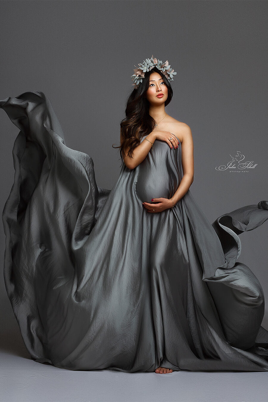 brunette model poses wearing a silky scarf against her body with a lot of fabric creating flying movements. she has a flower crown to match the style.