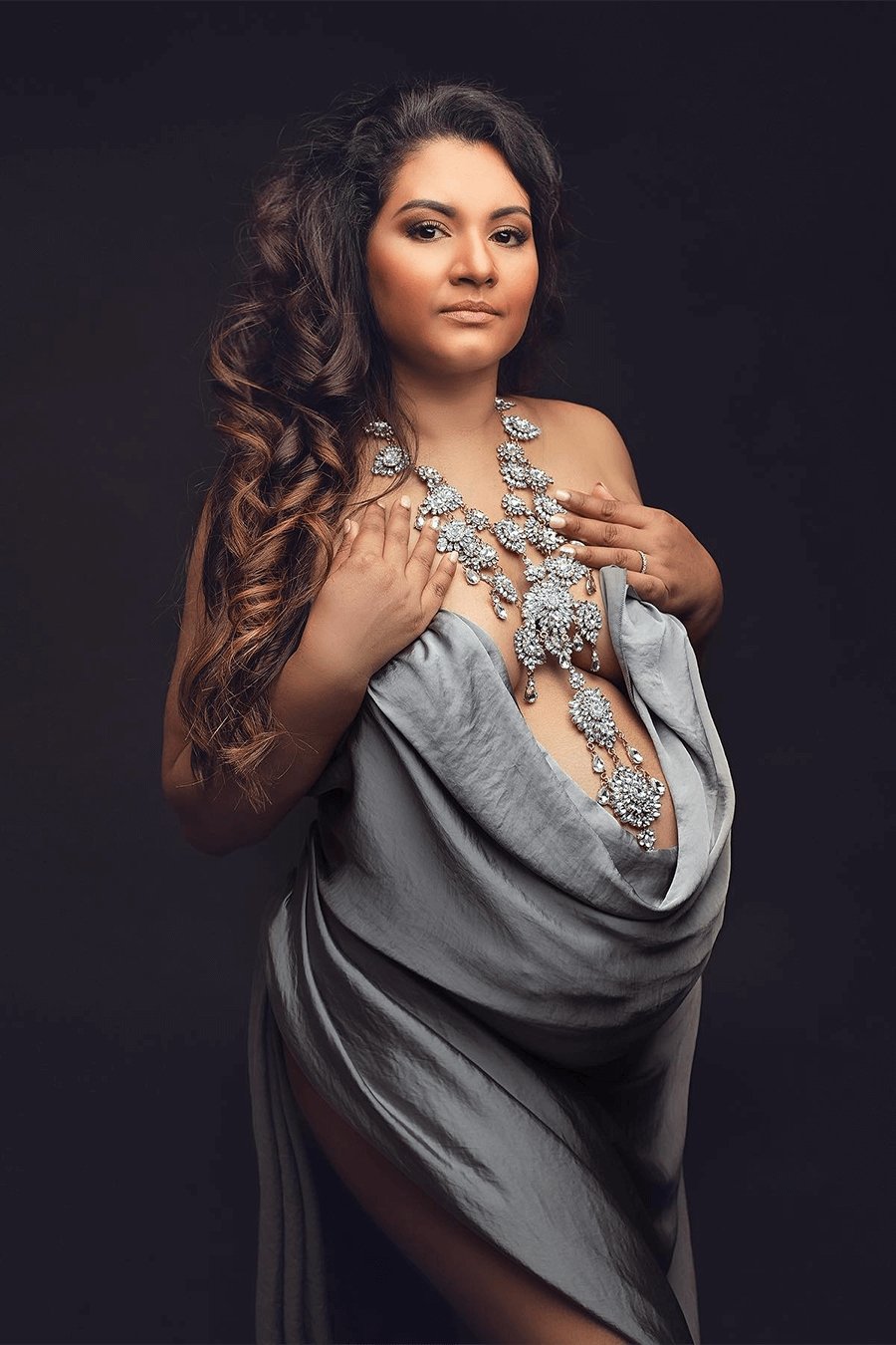brunette model covers her body with a grey silky scarf. she has a long large silver necklace.