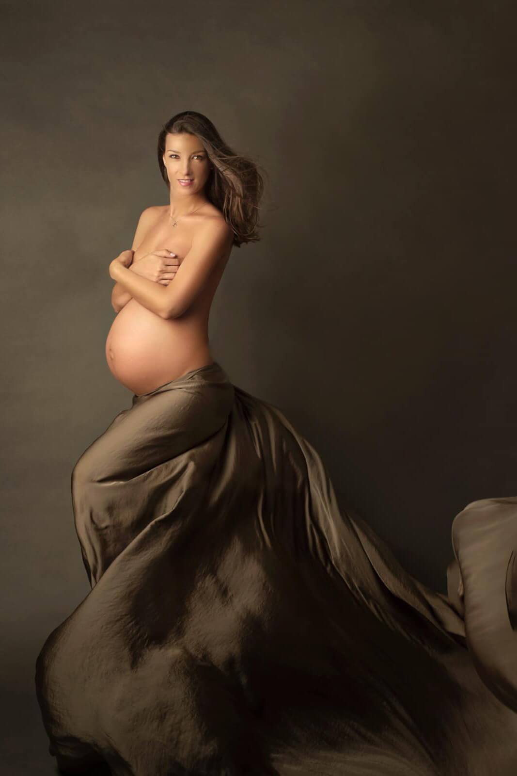 A pregnant woman is posing in a studio. she is wearing the silky scarf olive as a skirt. the fabric is tied around her waist.