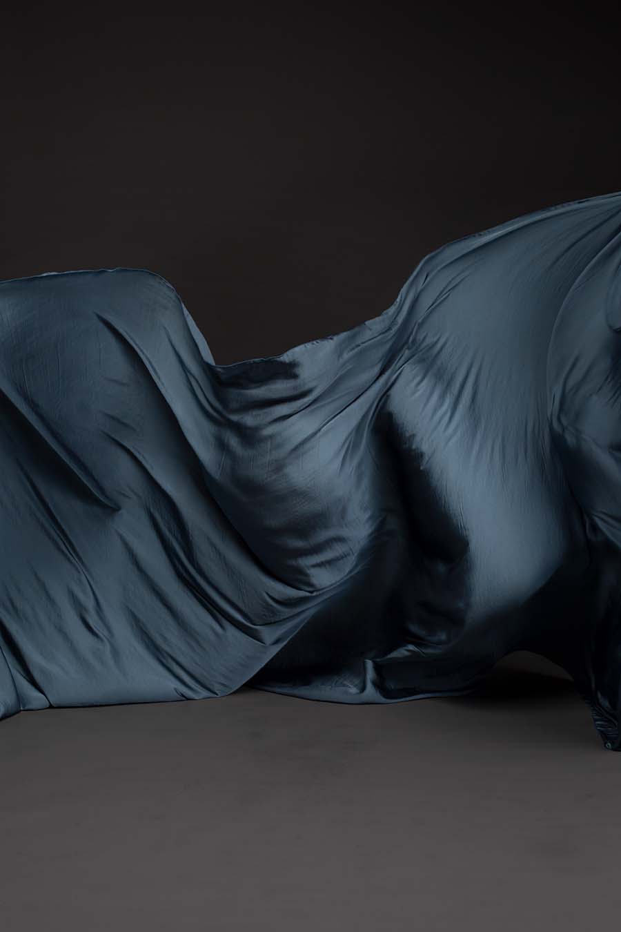 Photo taken on a studio and shows only the mii-estilo silky scarf in steelgrey color. The photo shows the scarf flying in front of the camera with playful movements.