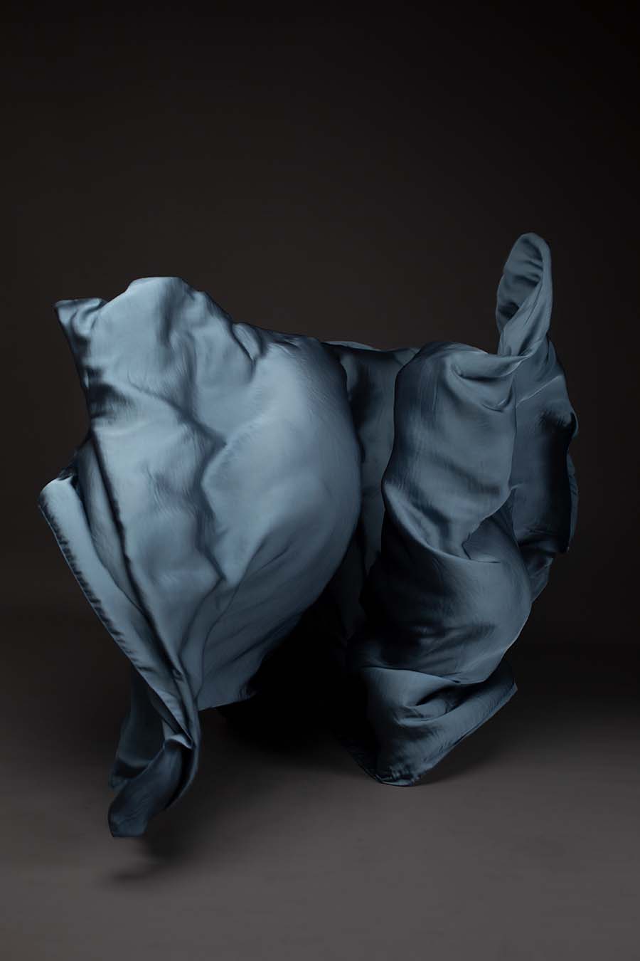 Photo taken on a studio and shows only the mii-estilo silky scarf in steelgrey color. The photo shows the scarf flying in front of the camera with playful movements.