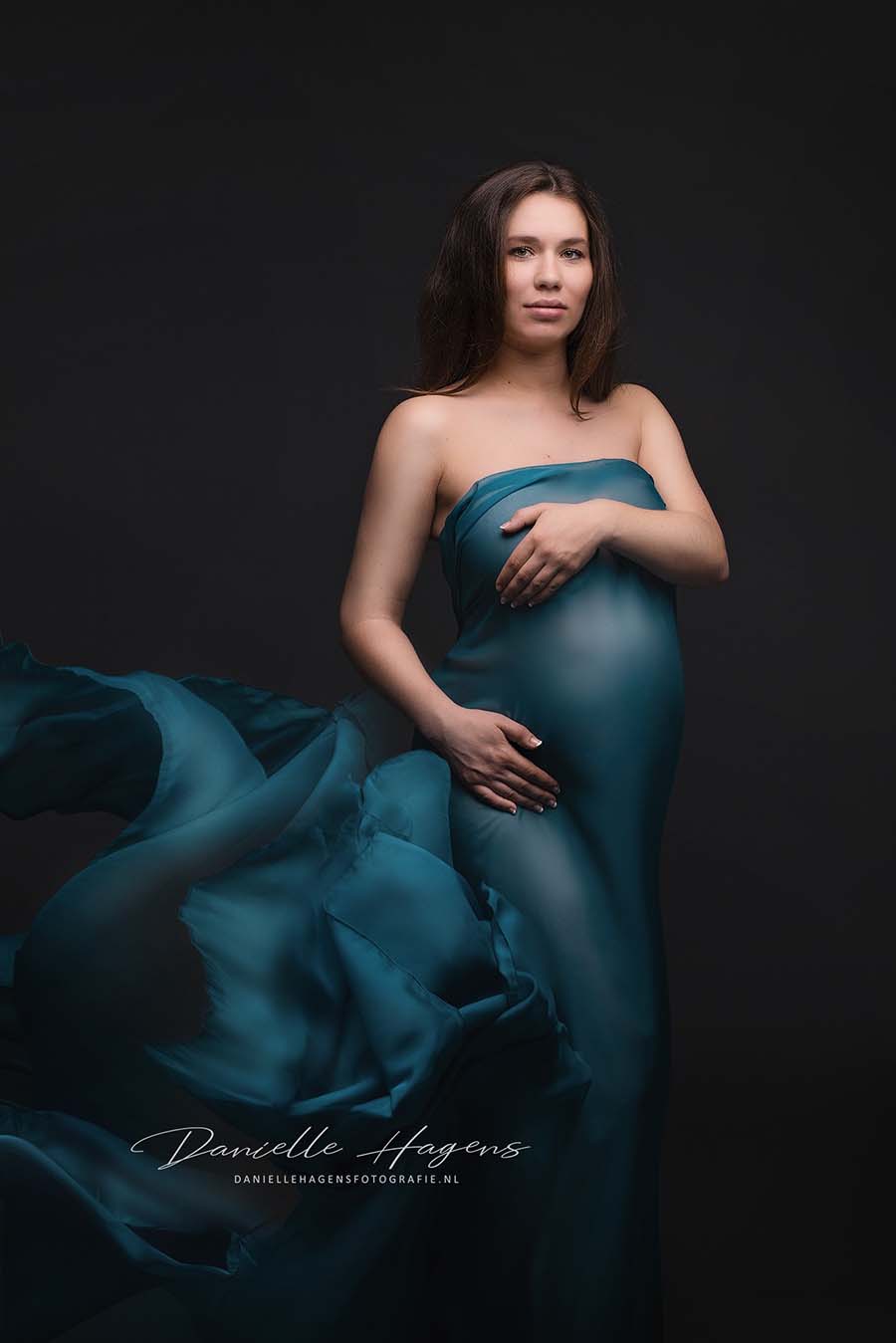 The pregnant woman is wearing a dress made out of the scarf. The scarf has a beautiful petrol colour