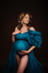 pregnant model poses in a studio with a tulle dress in petrol color. the dress has a one shoulder top. one of the shoulder have a big tulle sleeve and a sweetheart neckline. the dress has a middle split on the skirt and a bodysuit underneath.