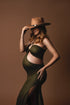 blond model poses in a studio wearing an olive maternity long dress with cut out details on the side and a keyhole peekaboo top. she has a hat to match the style. 