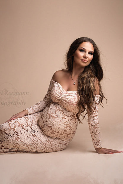The model is sitting an the floor and leaning on her hand. She is wearing a tight off the shoulder dress that is made out of lace. The colour is pink