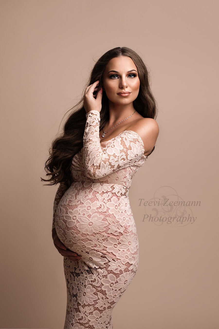 This long off the sholder dress is made out of lace . The model has long brown hair and she is pregnant
