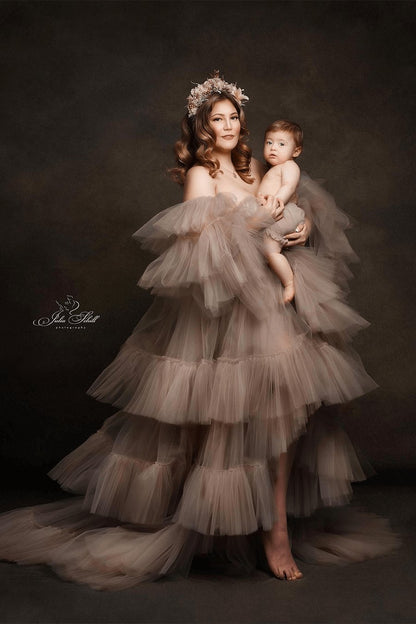 mother poses in a studio together with her kid. she is wearing a large tulle dress in sand color and a flower crown on her head.