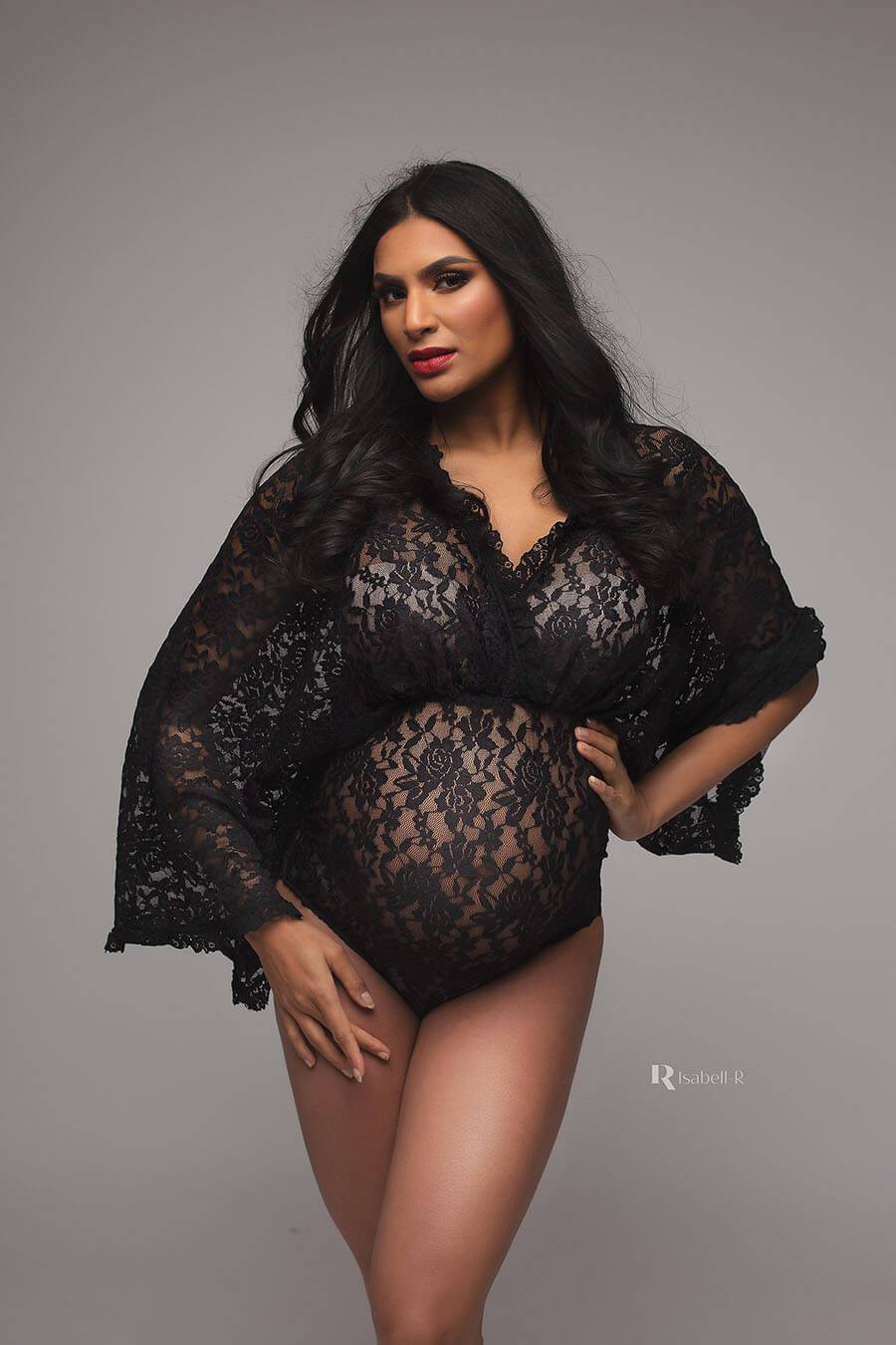 A pregnant woman is wearing a black lace bodysuit, The top is boho styled and see trough. She is wearing her own bra underneath