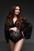 Pregnant model with long hair wears a maternity bodysuit during a photoshoot. The bodysuit is made of lace and features a low-v cut and kaftan sleeves top. The model looks to the side while holding her bump and waist. The photo is taken in a studio.