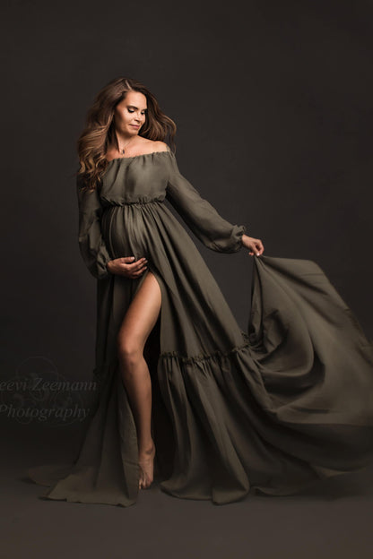Dark blond pregnant model poses in a studio wearing a mii-estilo boho style dress in olive color. She stands tall and faces the side with her eyes partially closed. One of her legs can be seen through the split on the skirt. She holds her bump with one hand and the skirt from the dress with the other one.