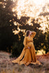 brunette model poses outdoors with a long ocre boho style dress.