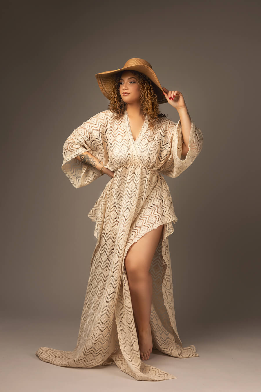 model poses in a studio wearing a western boho chic dress in ecru color. the dress is made of a special boho lace fabric. the model has a brown hat to match the style. 