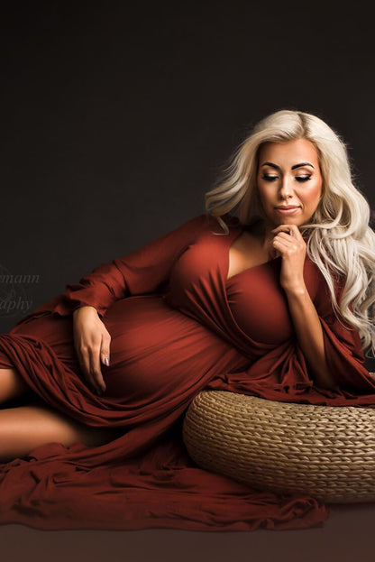 Blond pregnant model laying on a studio during a maternity photoshoot. She has her eyes partially closed and has on hand on her chin and the other resting on her baby bump. 