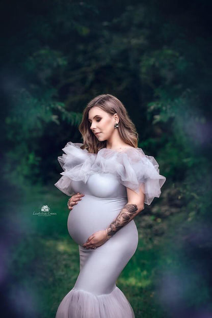The pregnant model is outside in the woods. The photo makes it look like you are seeing her trough the plants and flowers. she is wearing a long grey dress. The dress is part tulle and part jersey.