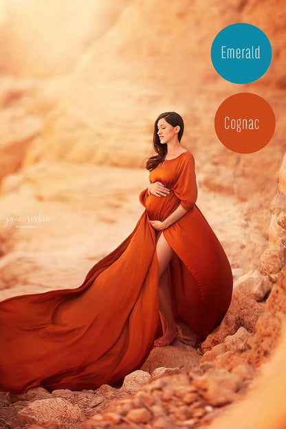 model poses outside by a rocky cliff wearing a maternity silky cape in cognac color. 