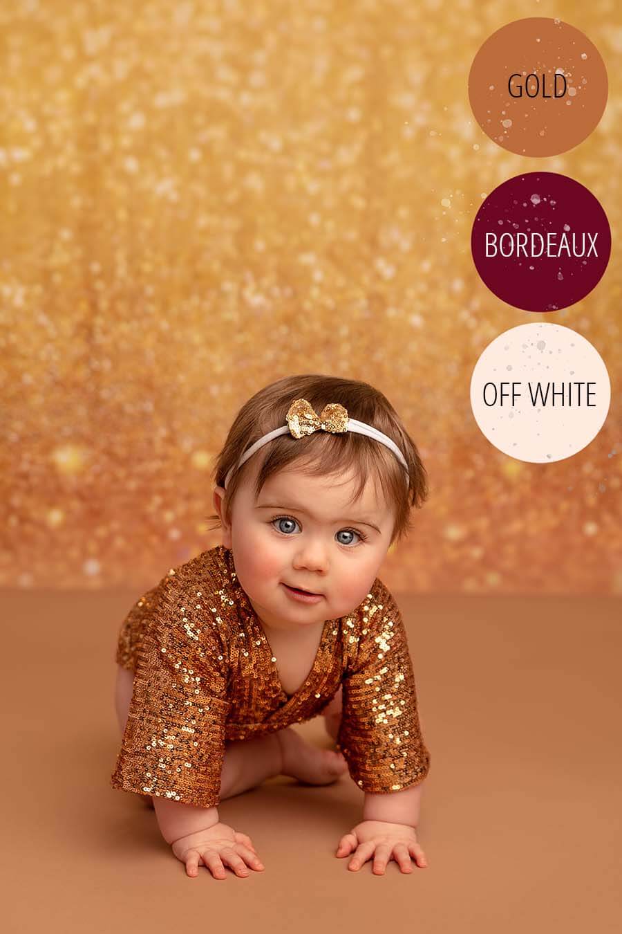 little baby girl poses in a studio wearing a glitter romper in gold color. she has a matching hairband. 