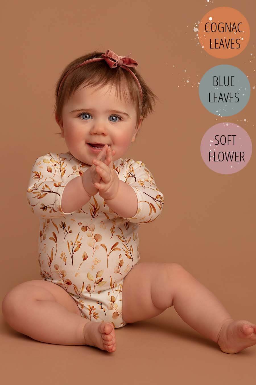 baby girl poses sitting and wearing a baby romper with long sleeves with leaves pattern in sepia tones.