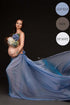 Pregnant brunette poses in a studio for a maternity photo session. She has a draping light blue fabric tied to her waist and holds a flower bouquet in front of her chest to cover her breasts. 