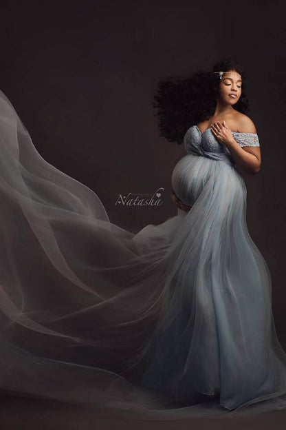 pregnant model poses in a studio with a light blue dress. the dress has a lace top and a tulle long skirt.