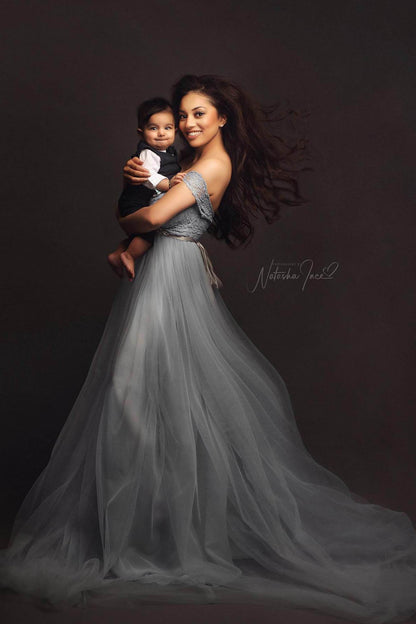 model poses with her kid wearing a light blue dress off shoulder with short sleeves. she and her baby are both smiling to the camera.