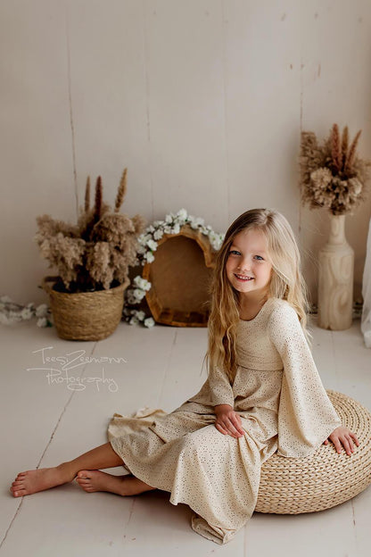 Little girl poses in a studio wearing a sand dress made of brocante jersey with long sleeves. Her hair is long and loose.