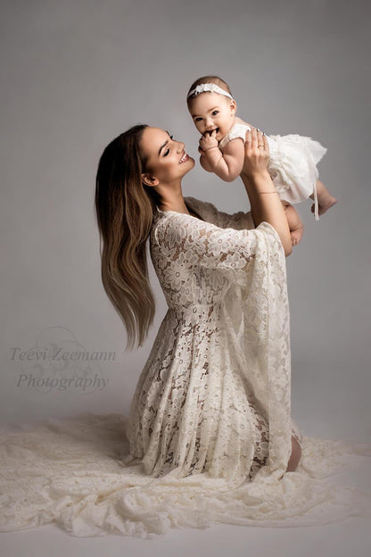 Woman poses in a studio holding and smiling at her baby girl. They are both dressed in an off white outfit made of lace.